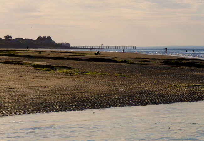 Coucher de soleil sur la plage de Lion sur Mer dans le Calvados avec des personnes qui marchent dans l'eau